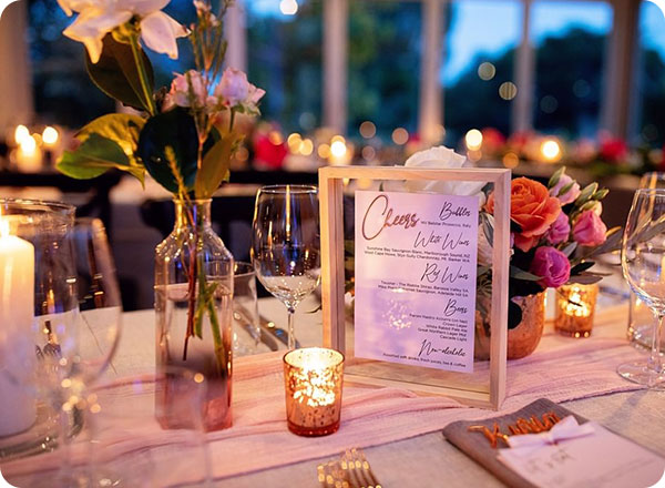 Photo is a close-up of a wedding tables smaller details including candles, flowers and drinks menu
