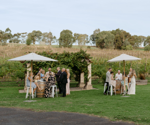 Wedding guests enjoying cocktail hour with umbrellas and wine barrels