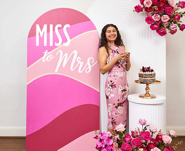 Woman standing next to a Miss to Mrs Backdrop Arch