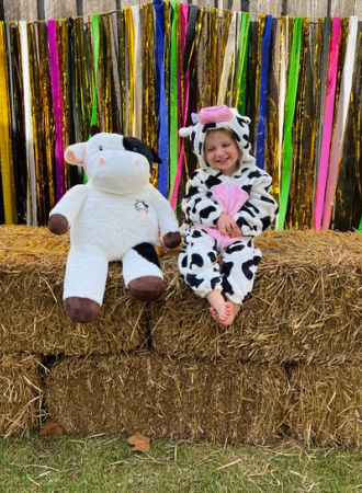 Little kid dressed in a cow costume posing on a stack of hay bales