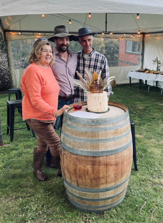 Guests posing behind a cake on a wine barrel at a birthday party