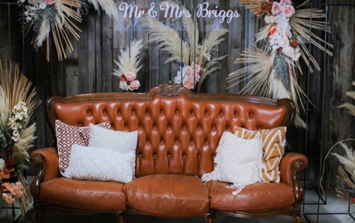 Photo shows a leather vintage couch surrounded by florals and a Mr & Mrs sign